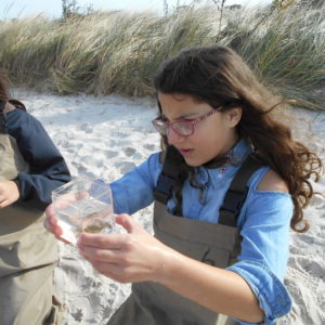 two girls on the beach looking at something in a glass