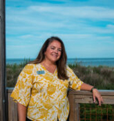 a woman standing next to a wooden fence near the ocean