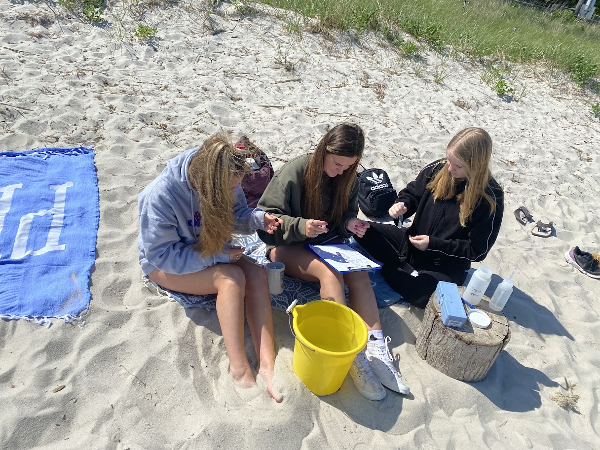 three girls sitting on the beach looking at their cell phones